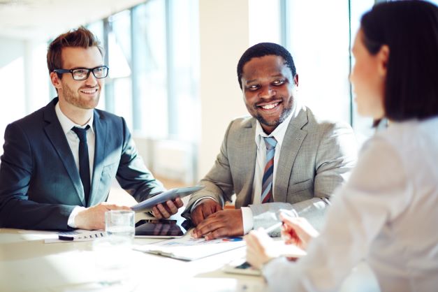 smiling-businessmen-listening-to-young-female-during-interview-SBI-300726714