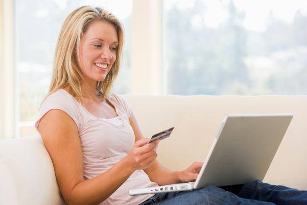 woman-in-living-room-using-laptop-and-holding-credit-card-smiling-SBI-301053177