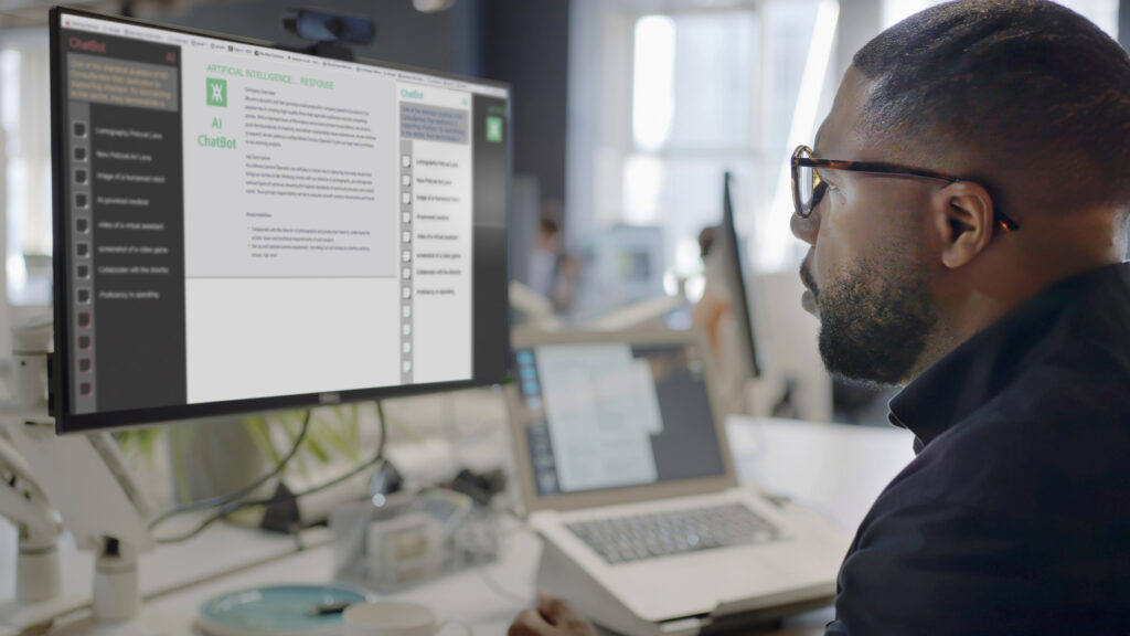 A man’s face looking into a computer screen in an open plan working office.